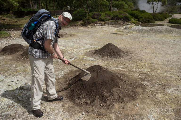 Mann demonstriert mit einer Hacke, wie die Töpfe mit dem Eintopf Cozido in der Erde vergraben werden.