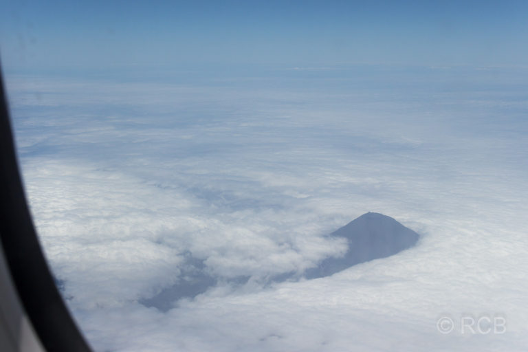 Blick aus dem Flugzeug auf den Gipfel des Pico, der aus den Wolken ragt.