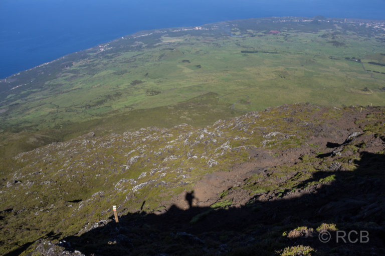 Schatten eines Wanderers am Hang des Pico mit Blick auf den Ort Madalena