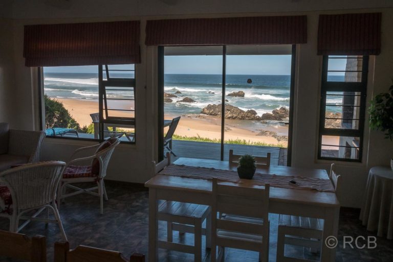 Inneres eines Ferienhauses mit Blick durch das Fenster auf Strand und Meeresbrandung