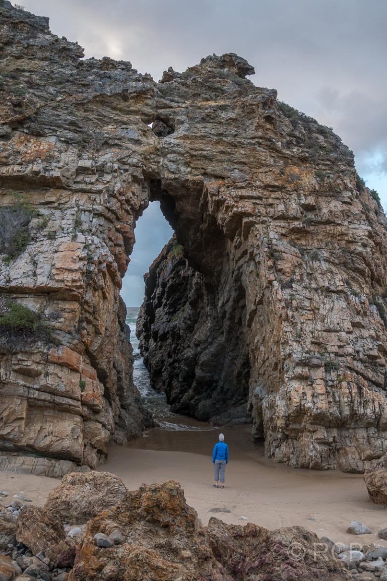 Winzig wirkender Mann unter dem großen Felsbogen des Arch Rock bei Keurboomstrand
