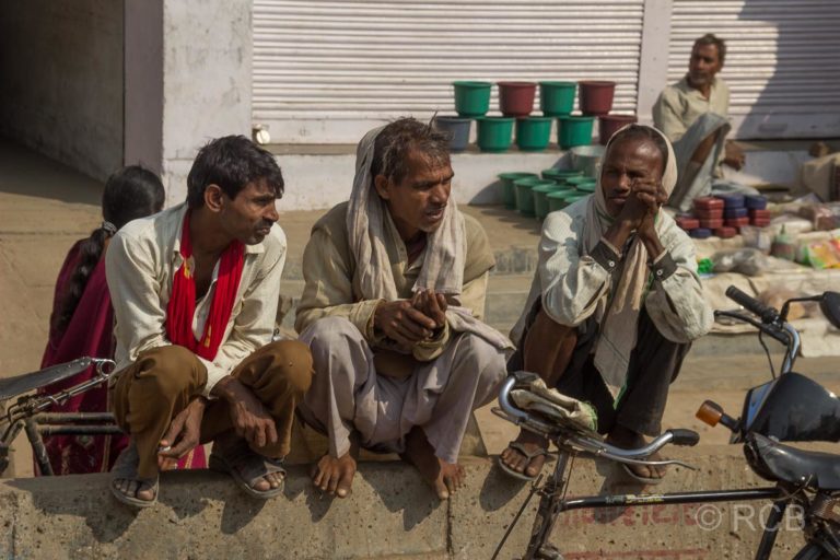 Männer hocken auf einer Mauer am Straßenrand auf der Fahrt durch Uttar Pradesh