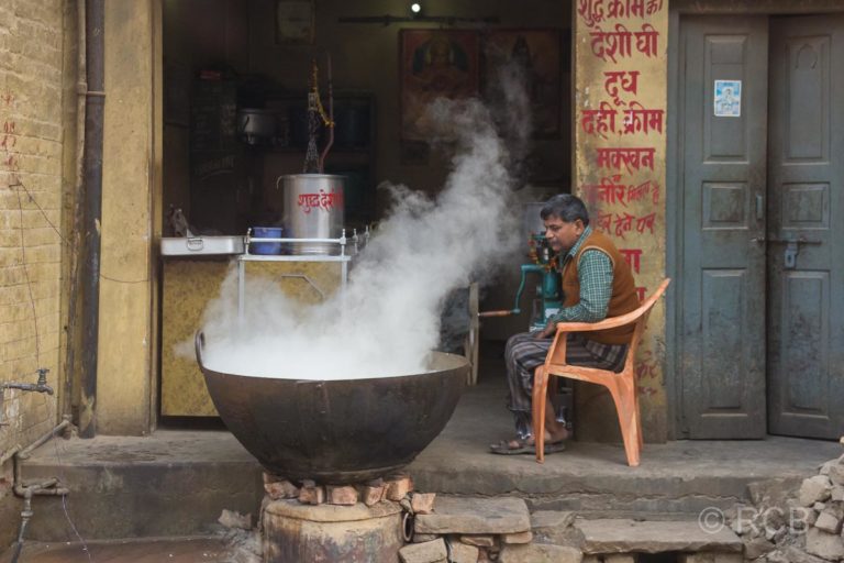 Varanasi, Mann erhitzt einen großen, dampfenden Kessel am Straßenrand