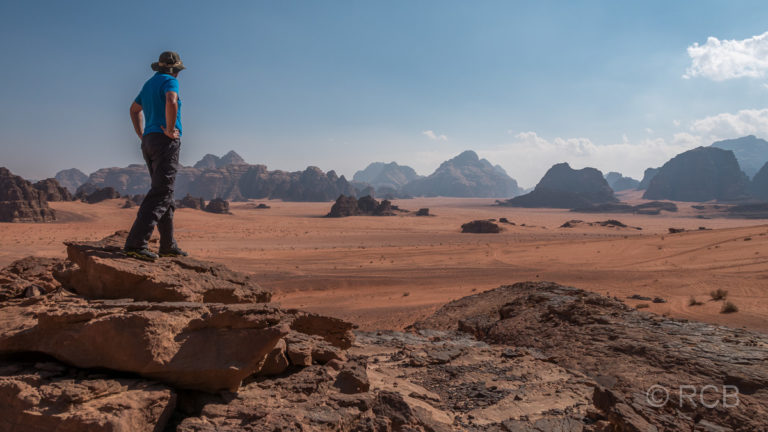 Mann überblickt das Wadi Rum von einem erhöhten Felsen aus