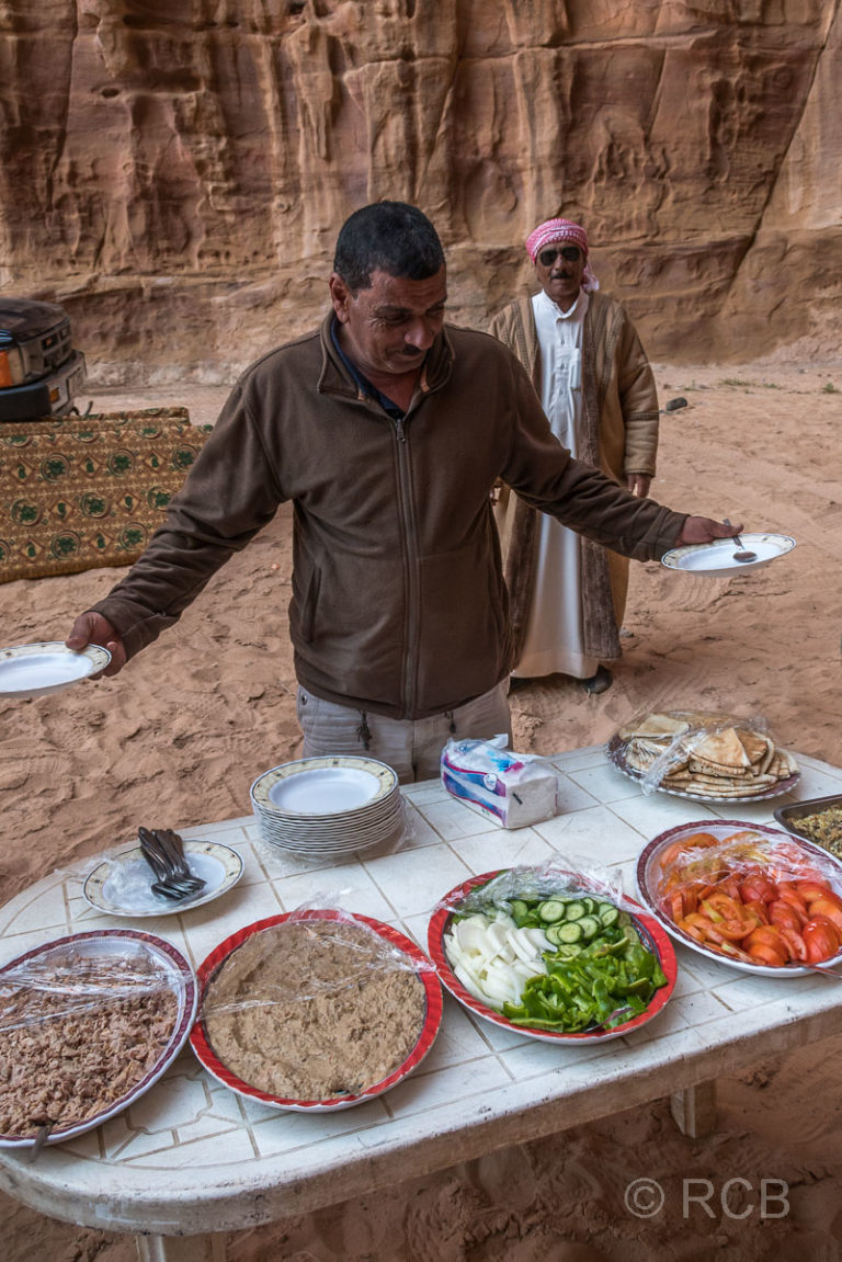Beduine präsentiert das Mittagsbüffet für eine Wandergruppe auf ihrer Rast im Wadi Rum
