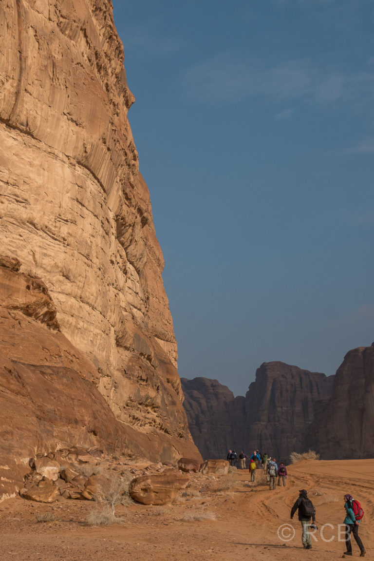 Wanderer passieren die Flanke eines riesigen Felses im Wadi Rum