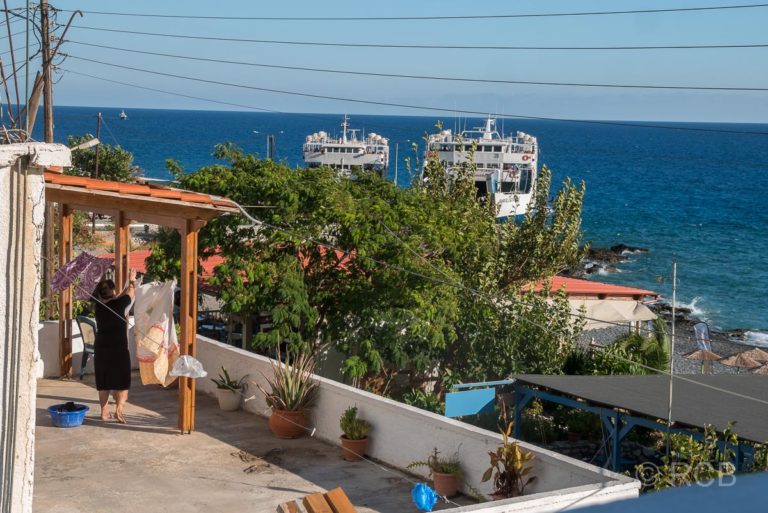 Blick von meinem Hotelbalkon auf den Fähranleger von Agia Roumeli mit 2 Fähren, im Vordergrund hängt eine Frau Wäsche auf ihrem Balkon auf