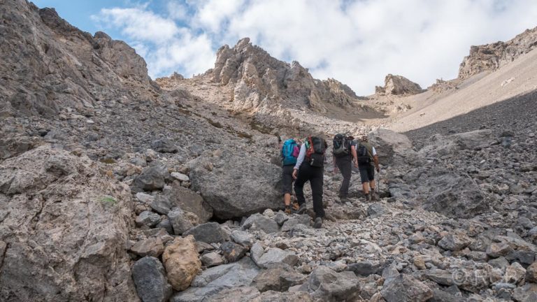 Wanderer steigen durch Geröll auf zu einem Bergsattel am Gingilos