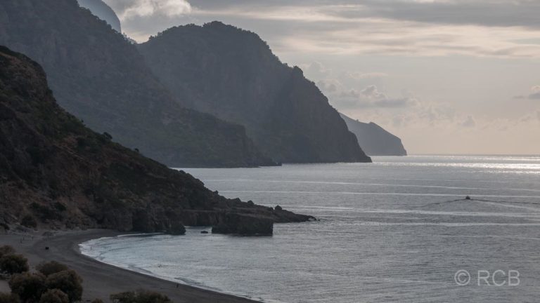 Blick entlang der Küste im Gegenlicht zum Kap Tripiti, ein einsames Boot fährt im Meer