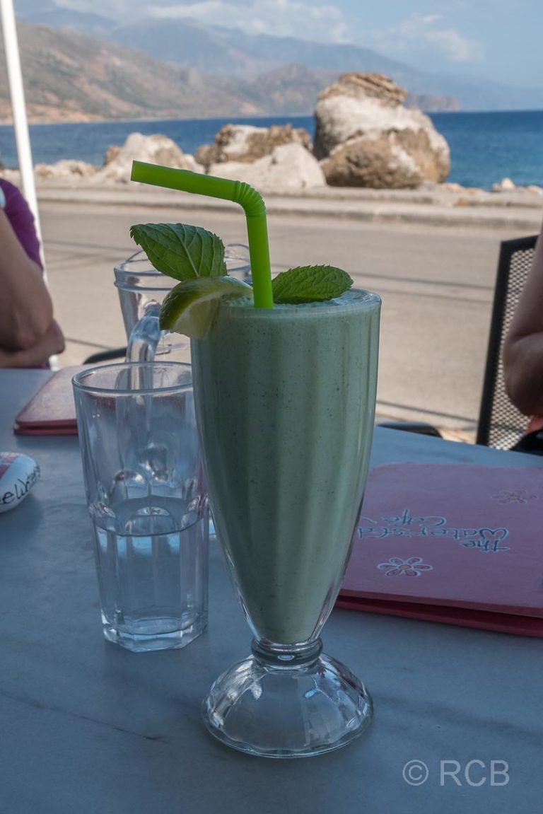 ein grüner Smoothie steht in einem Lokal mit Blick auf's Meer auf dem Tisch