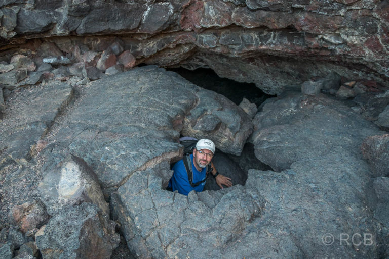 Mann klettert aus einem Loch am Ausgang des Indian Tunnel, Craters of the Moon NM