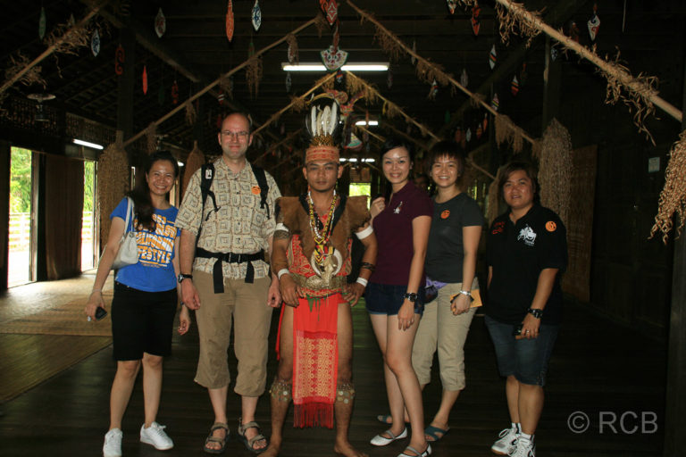 Touristen und ein Malaye in Stammestracht lassen sich fotografieren im Sarawak Cultural Village