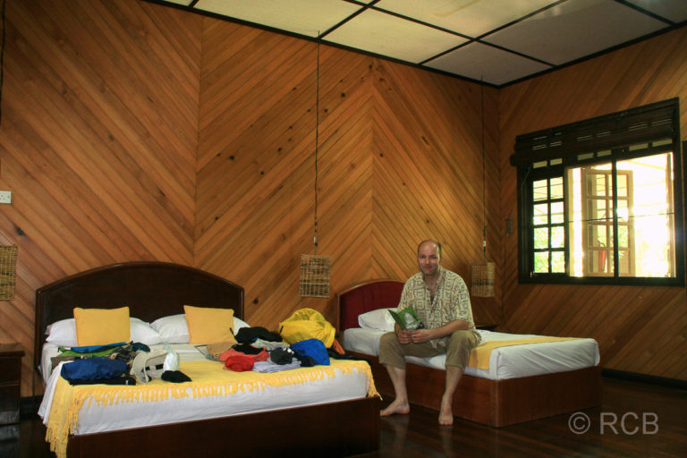 Mann sitzt auf einem Bett in seinem Gästezimmer in einem umgebauten "Longhouse", Mulu Nationalpark